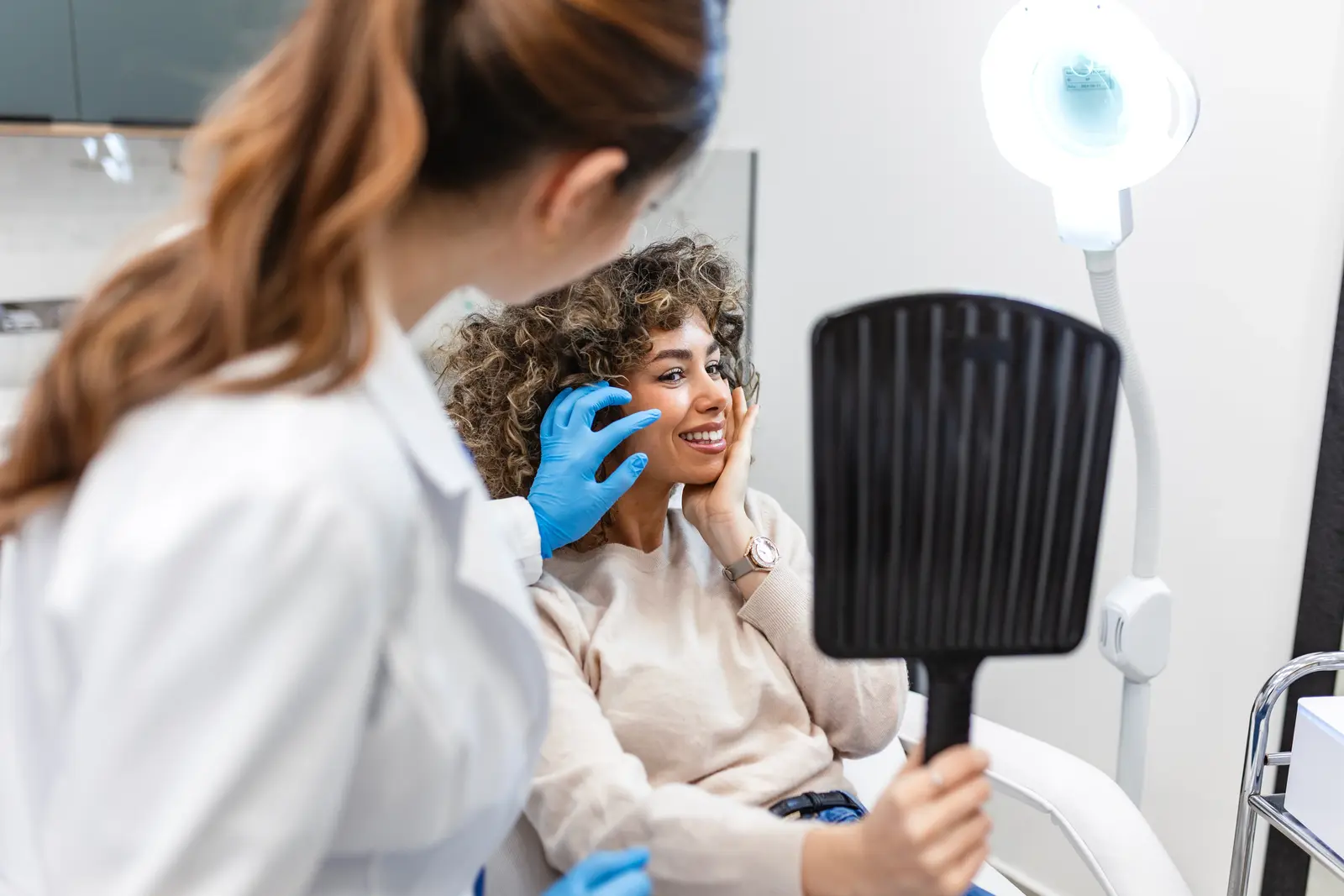 Patient smiling while holding mirror during facial treatment consultation.
